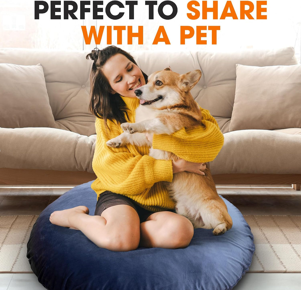Person kneeling on a navy round floor pillow hugging a corgi in a living room setting