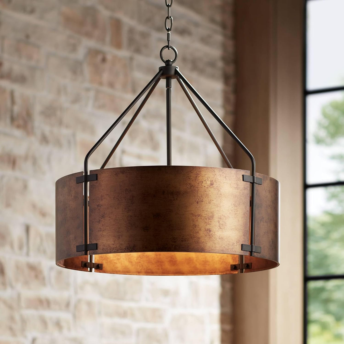Rustic bronze drum pendant angled close-up showing metal shade, hanging chain, and brick background