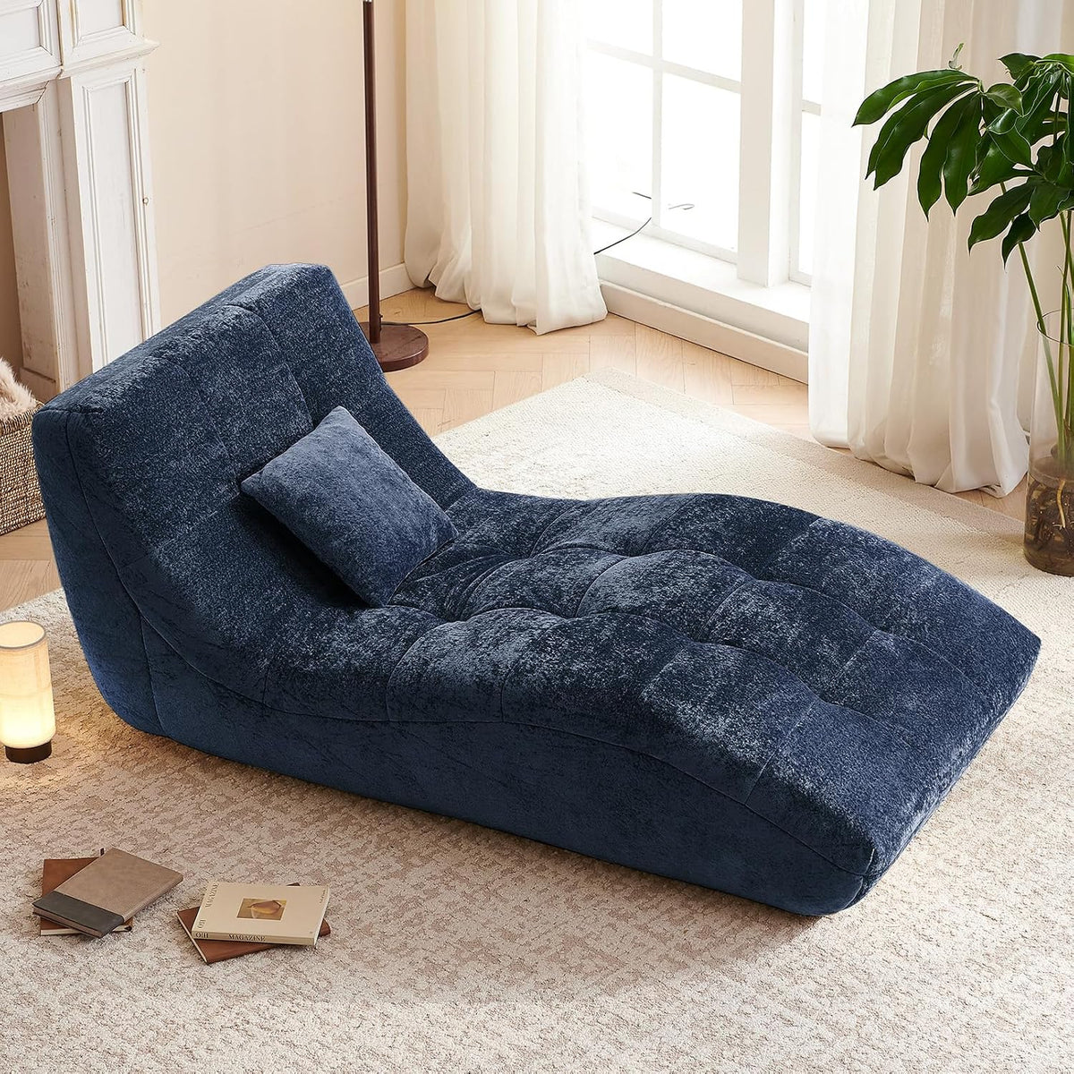 Navy blue chaise placed in a light-filled room with a plant and small lamp nearby.