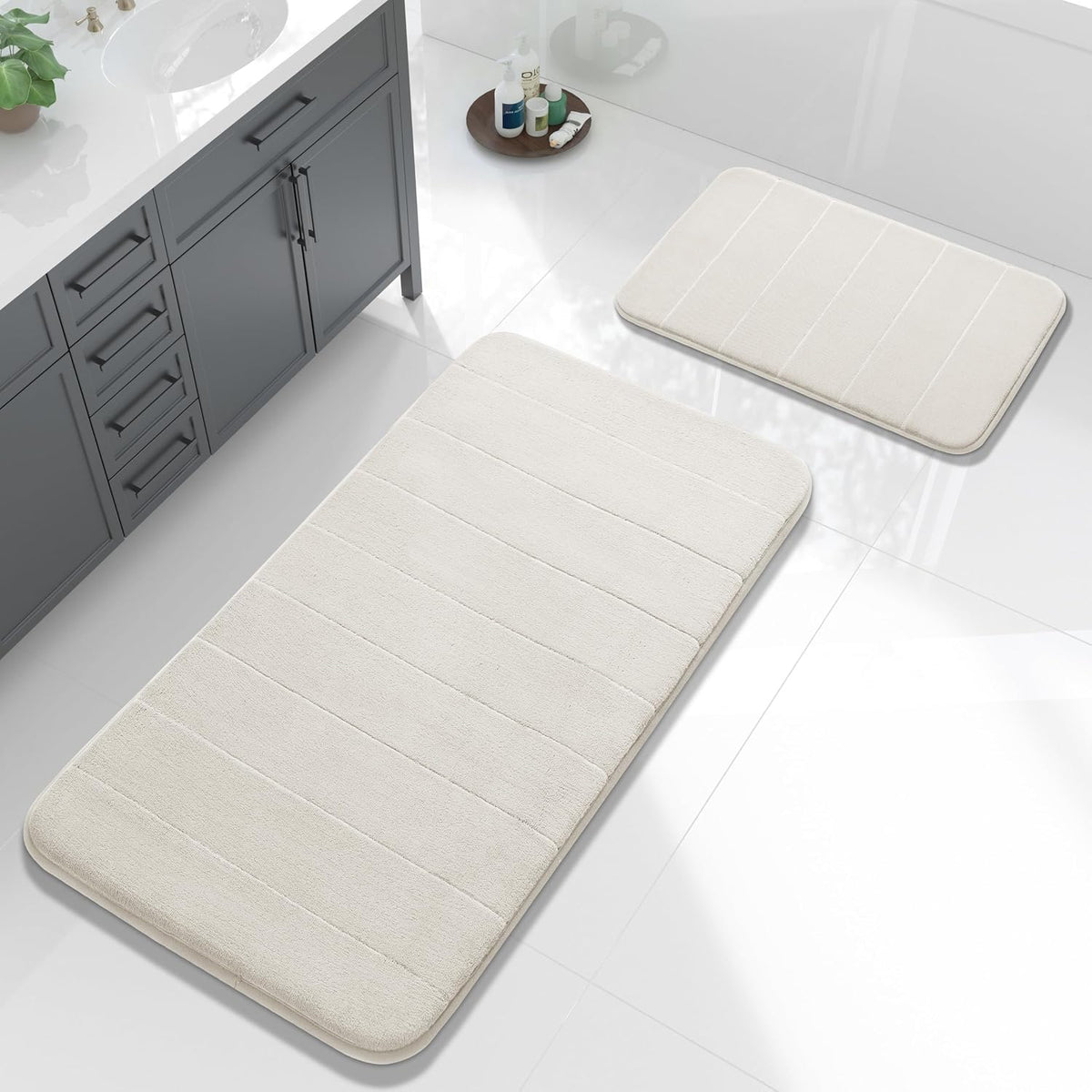 Cream/ivory bath mat pair on glossy tile beside a sink cabinet and tub accessories