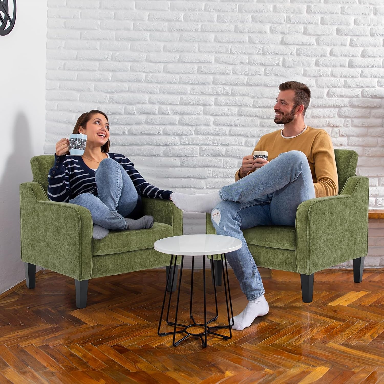 Two people seated separately on matching green armchairs facing each other with a small round table.