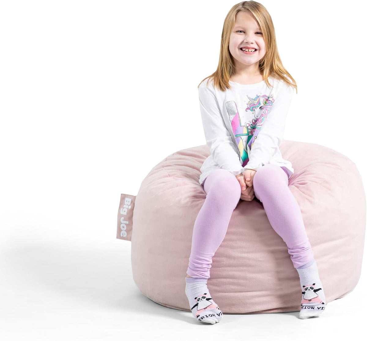 Smiling young girl sitting on a pale pink round bean bag, sitting forward on the cushion.
