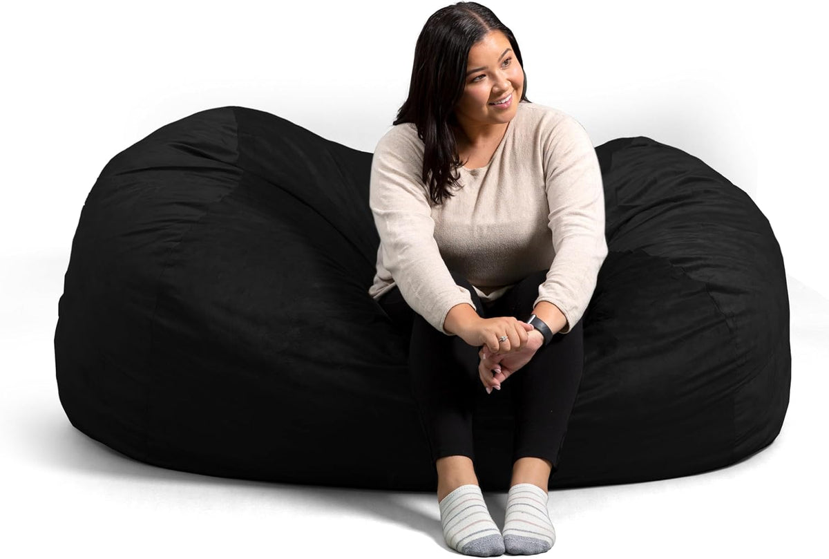 Woman sitting on a large black oversized bean bag chair against a white background.