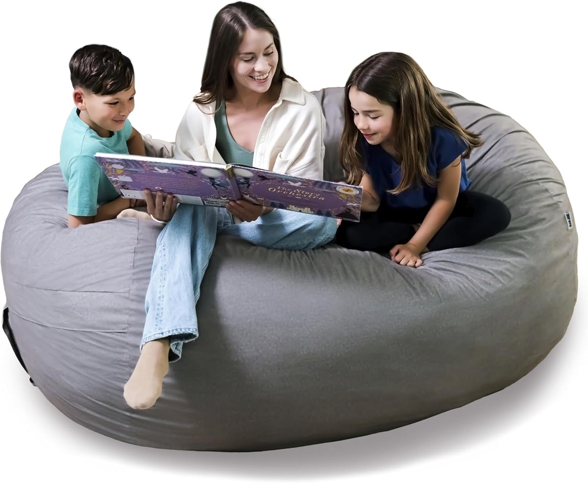 Three people — an adult reading to two children — seated together on a large light-gray lounger with a visible black carry