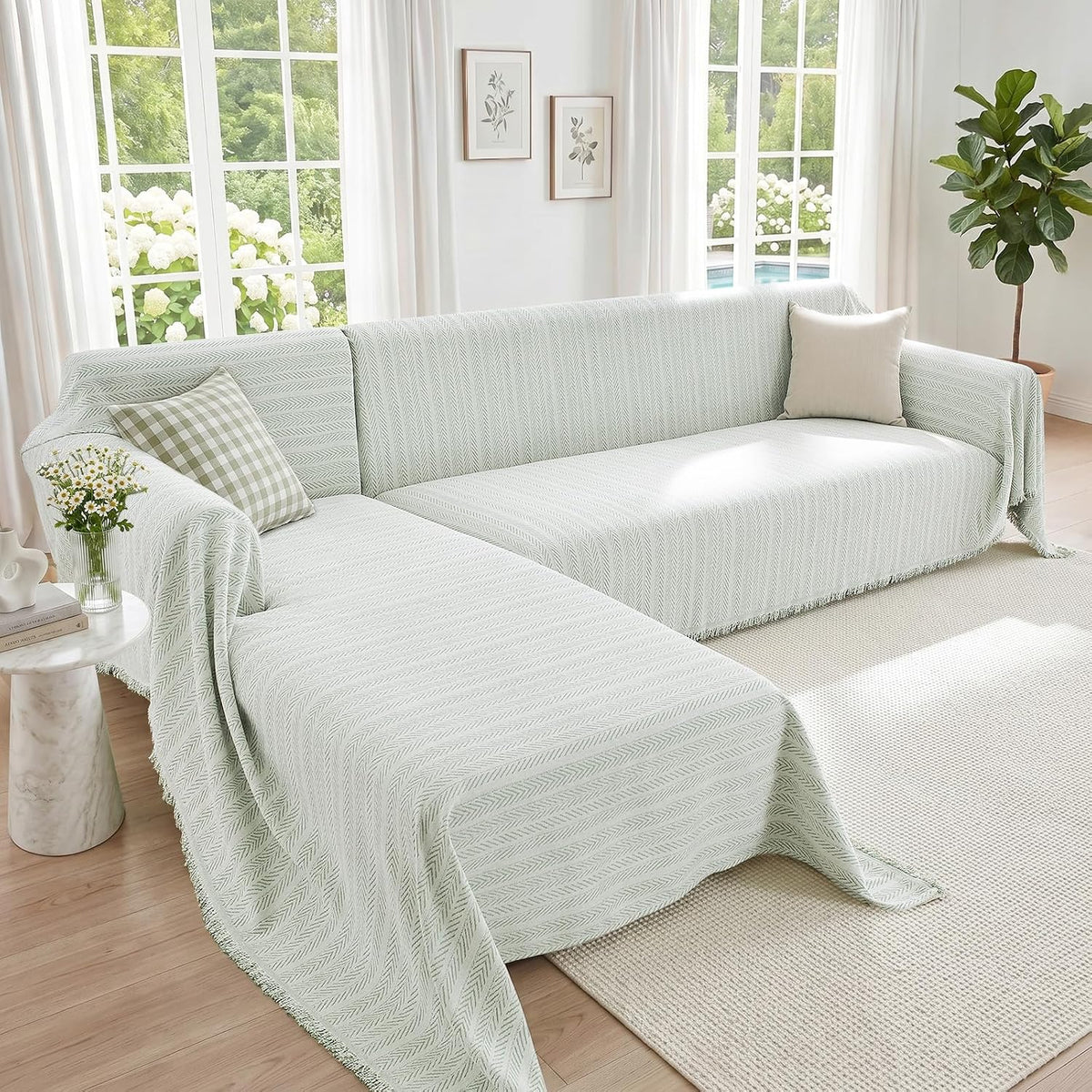 L-shaped sectional draped in a pale mint herringbone cover with a green gingham pillow and vase of daisies.