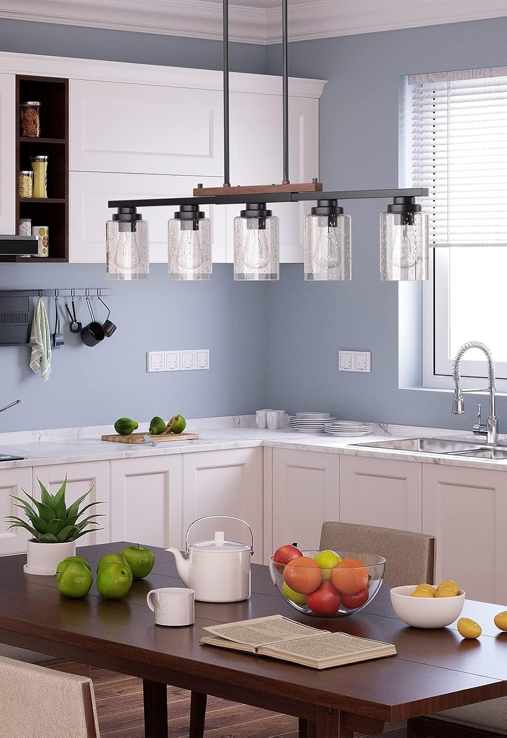 Five-light seeded-glass pendant above a wood dining table set with a teapot, open book and fruit bowl in a bright kitchen