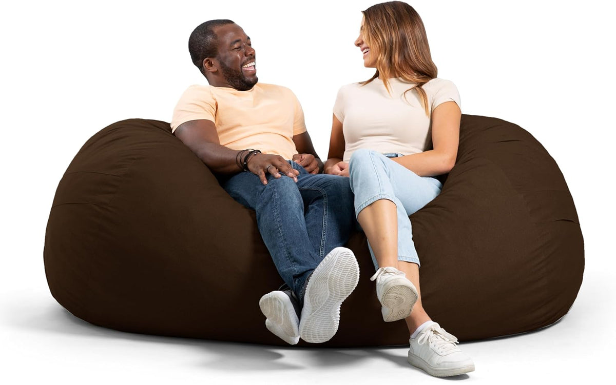 Two adults laughing while seated together on a giant brown oversized lounger from the front.