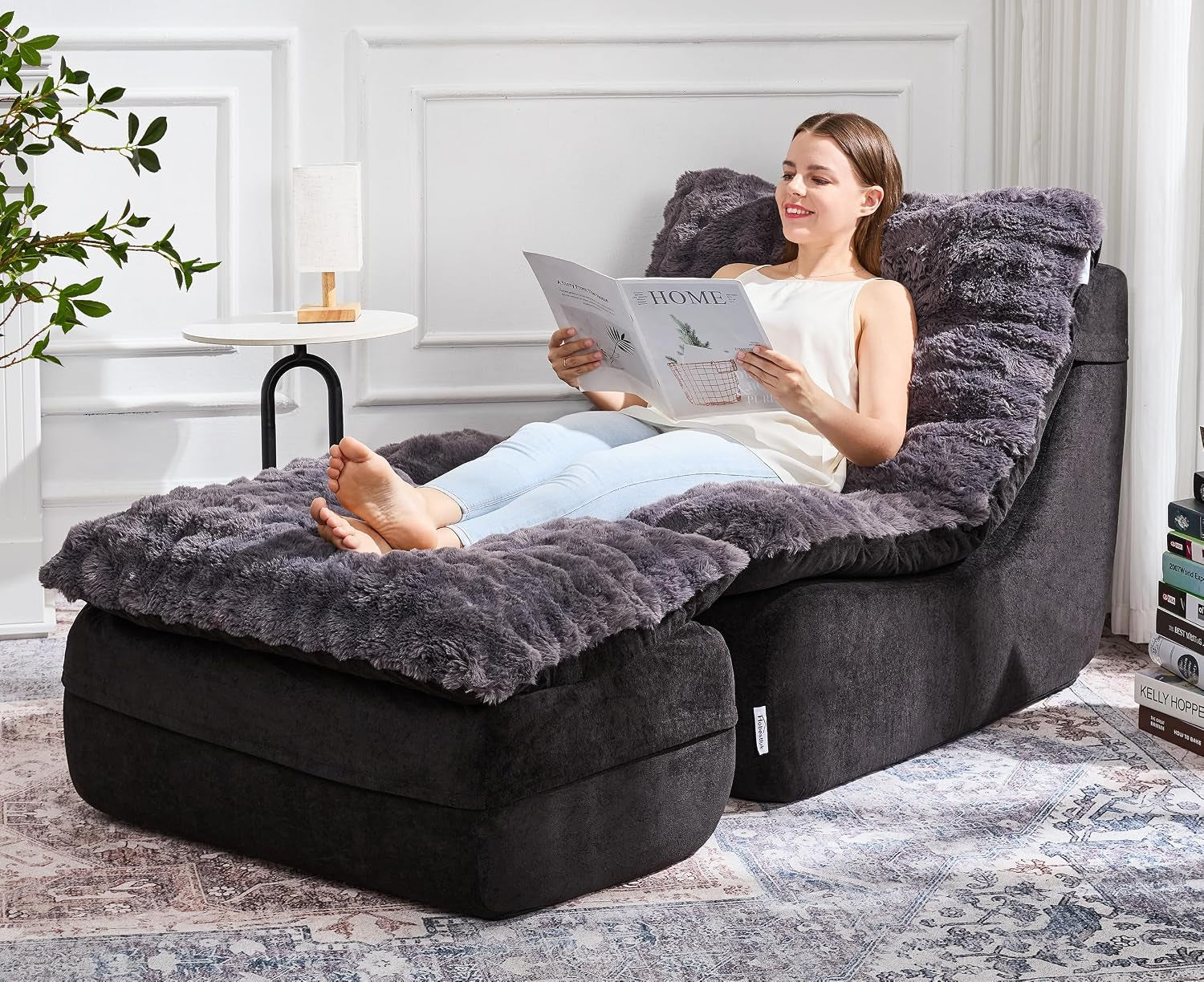 Woman reclining on a dark gray fluffy floor sofa and ottoman, reading in a bright room with side table and rug.