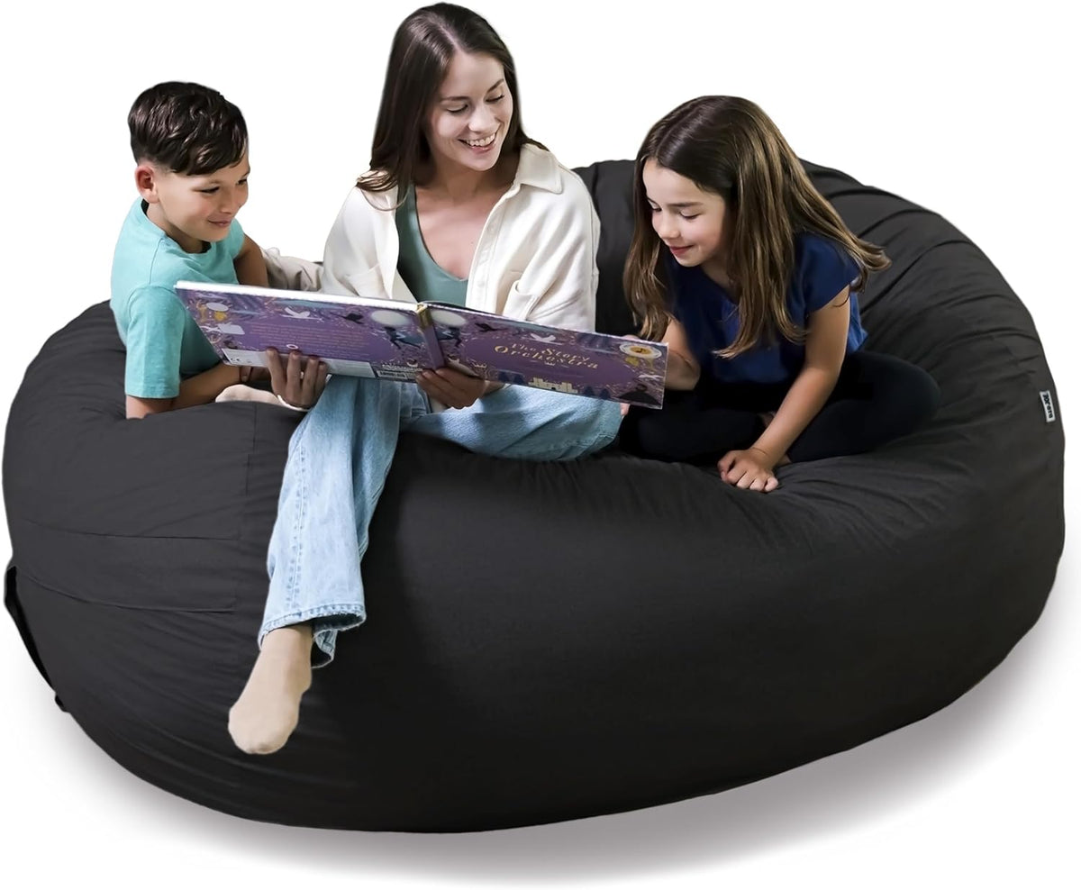 Three people sitting on a huge black round bean bag chair reading a book