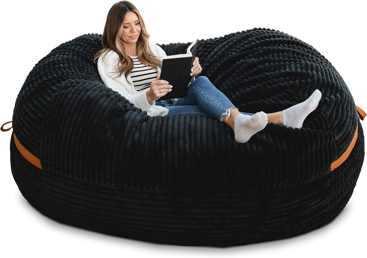 Wide angled side view of a black ribbed oversized lounger with a woman reading, showing low profile and tan carry handles.