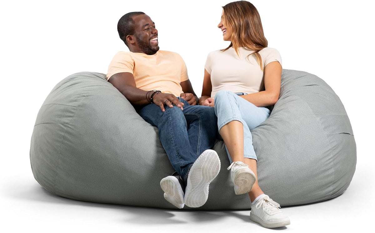 Man and woman laughing together while seated on a large light gray lounger, feet extended forward.