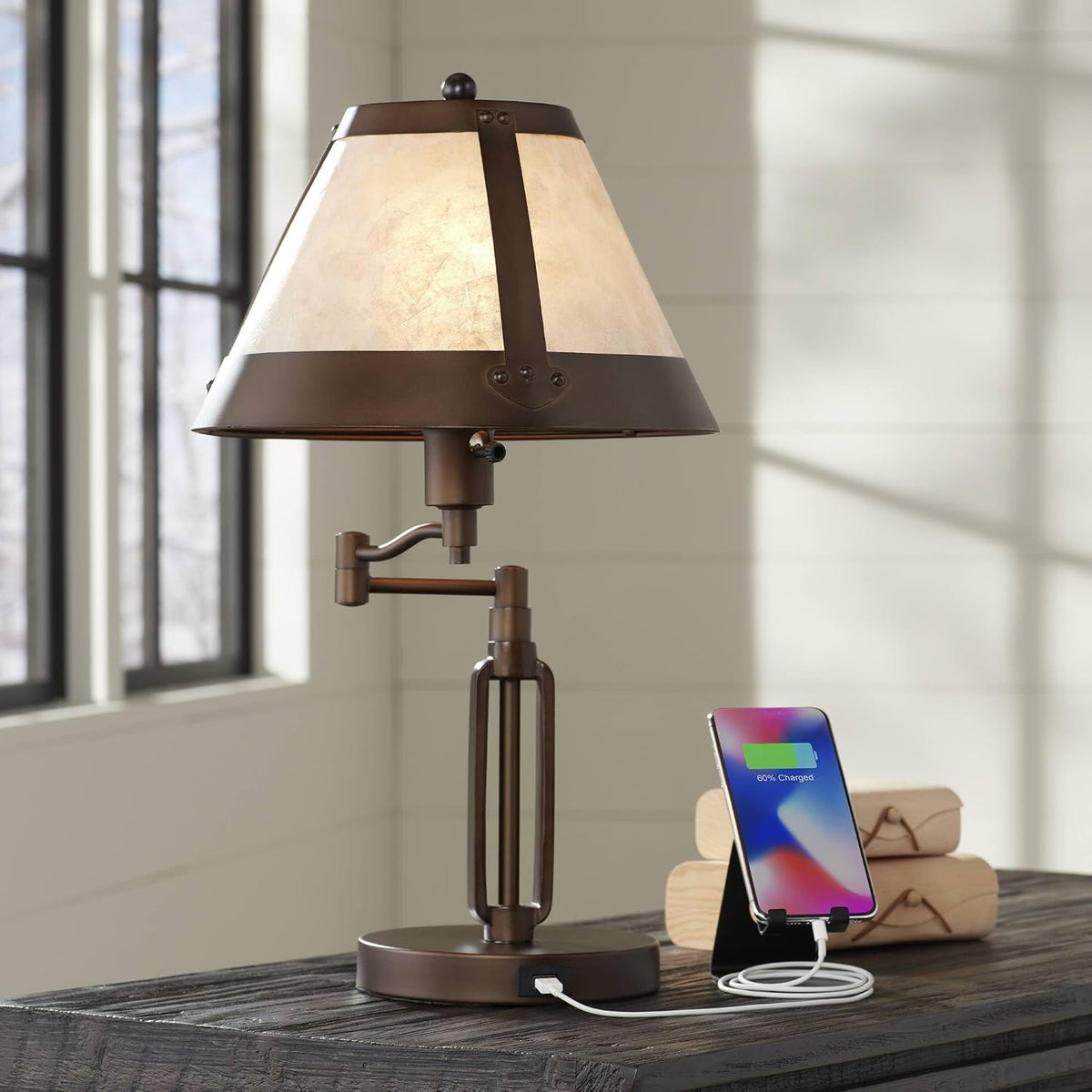 Bronze desk lamp with mica shade angled front view on a wooden desk with a charging phone