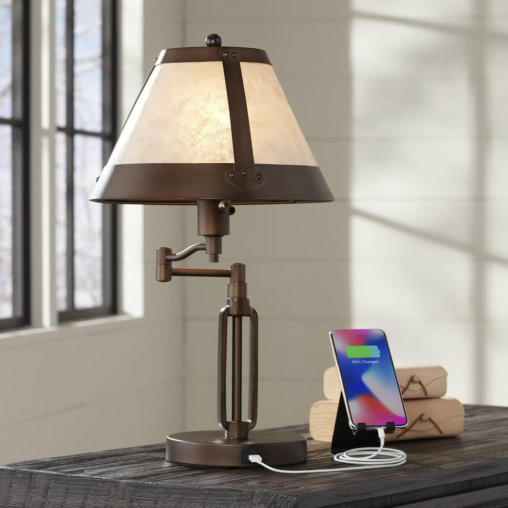 Bronze desk lamp with mica shade angled front view on a wooden desk with a charging phone
