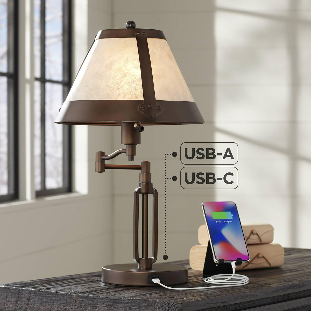 Lit lamp on a wooden table by a window with a phone on a stand and stacked wooden boxes beside it.