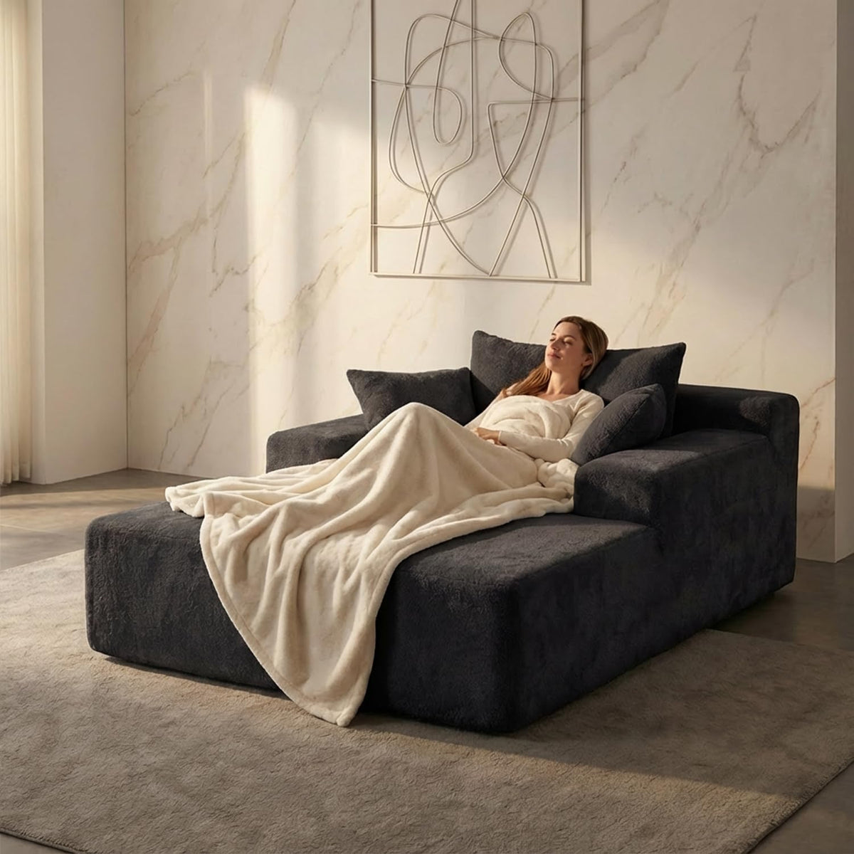 Charcoal chaise converted to a wide bed with a woman reclining against back cushions under a soft throw.
