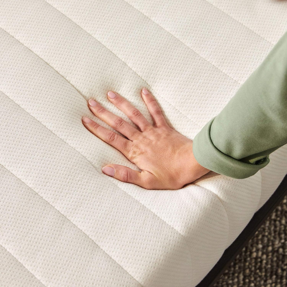 Hand pressing the mattress surface to show medium-firm indentation and quilted cotton cover texture.
