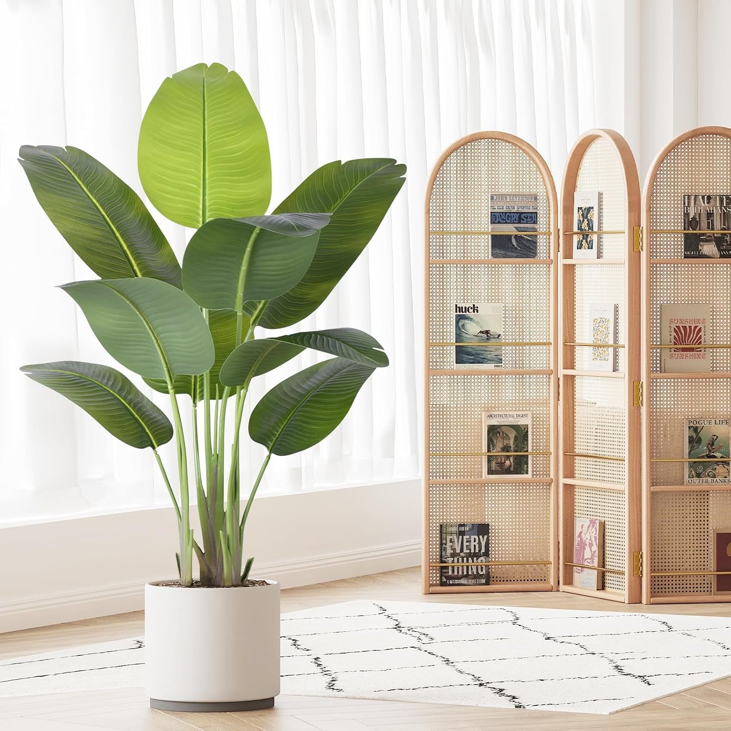 4ft Bird of Paradise faux plant in a round white pot on a rug with a folding room divider and bright curtains