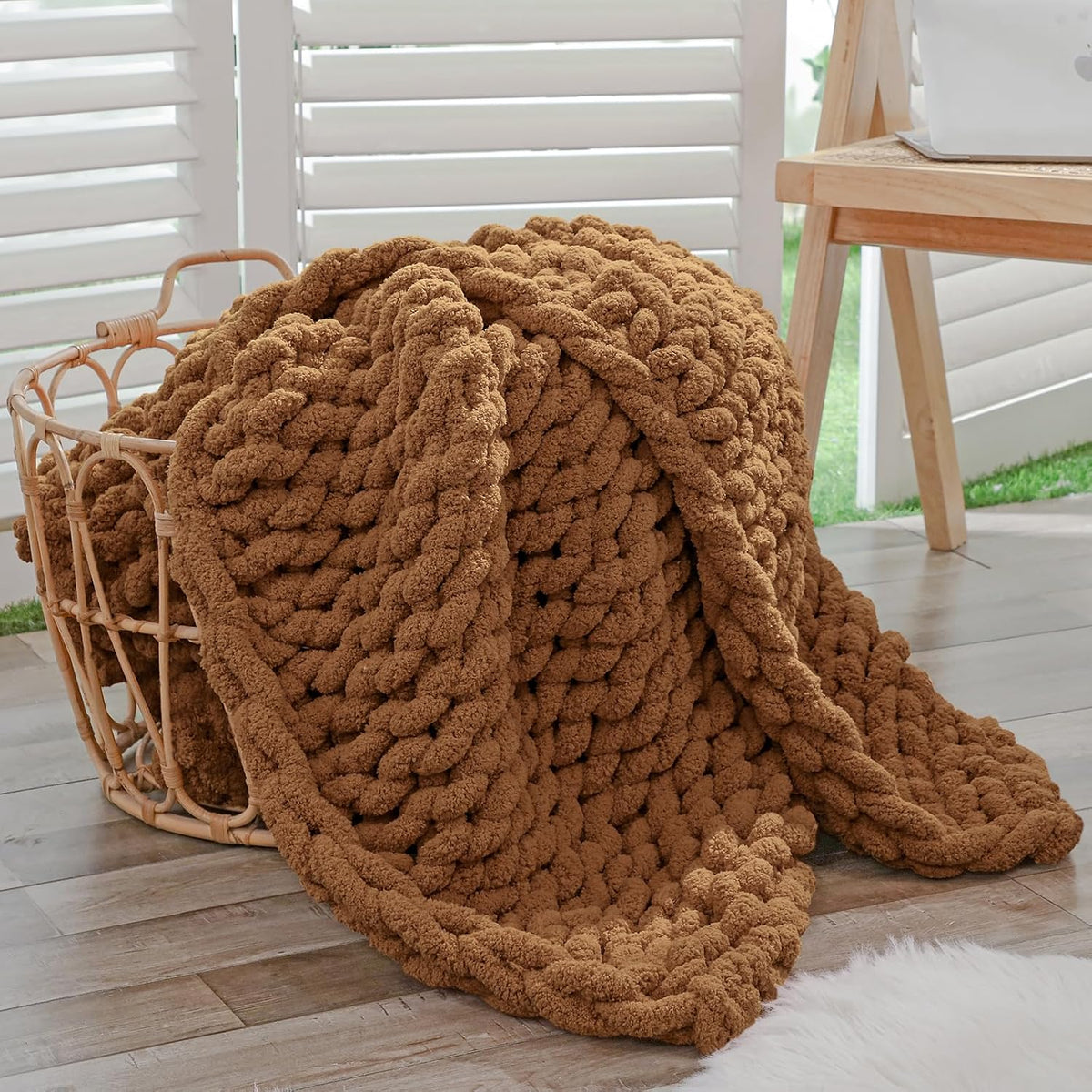 Brown chunky knit throw piled inside a woven basket beside a wooden desk.