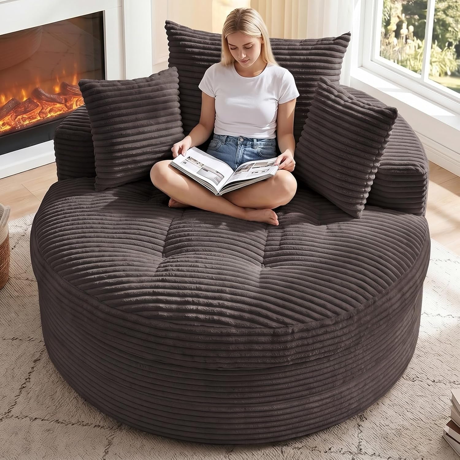 Top-front view of the round corduroy chaise in dark gray with three matching pillows and a person reading.