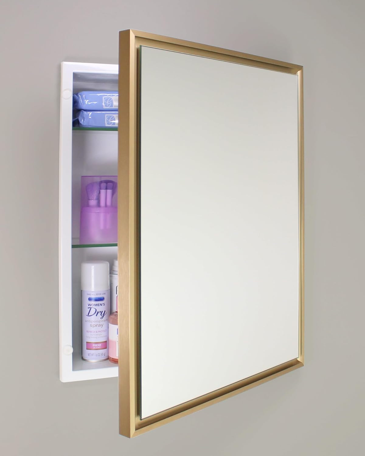 Gold framed recessed medicine cabinet angled front view mounted on a grey wall with the mirror door partially open