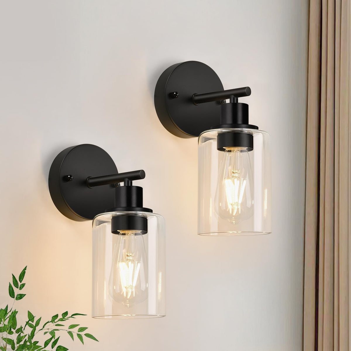 Two black wall sconces with clear cylindrical glass shades and lit filament bulbs.