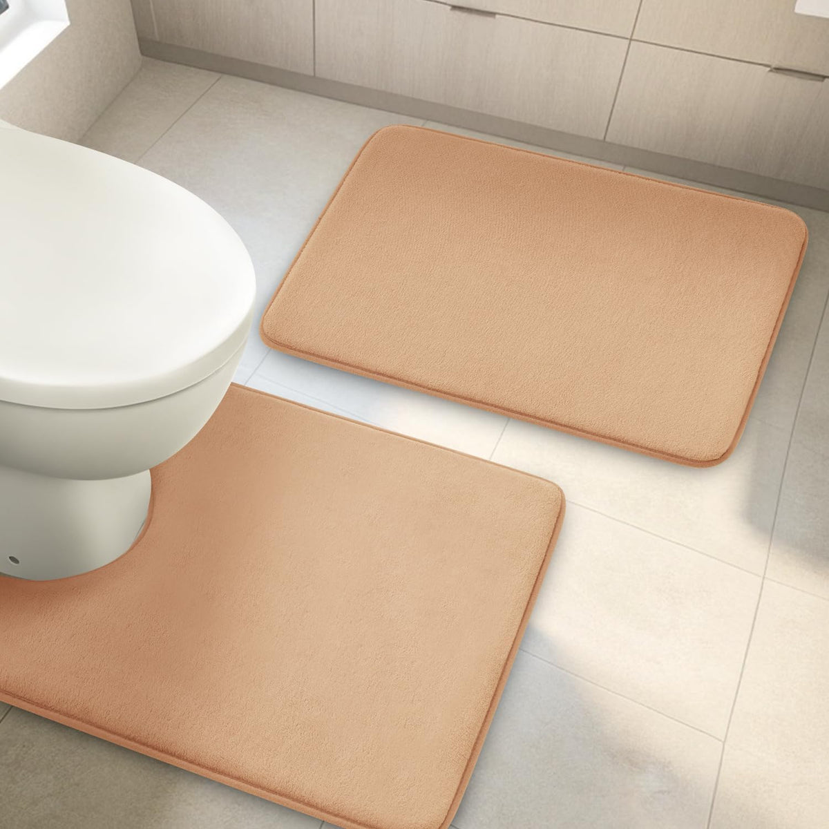 Top-down view of two peach-colored rectangular bath rugs near a toilet on light tile floor.