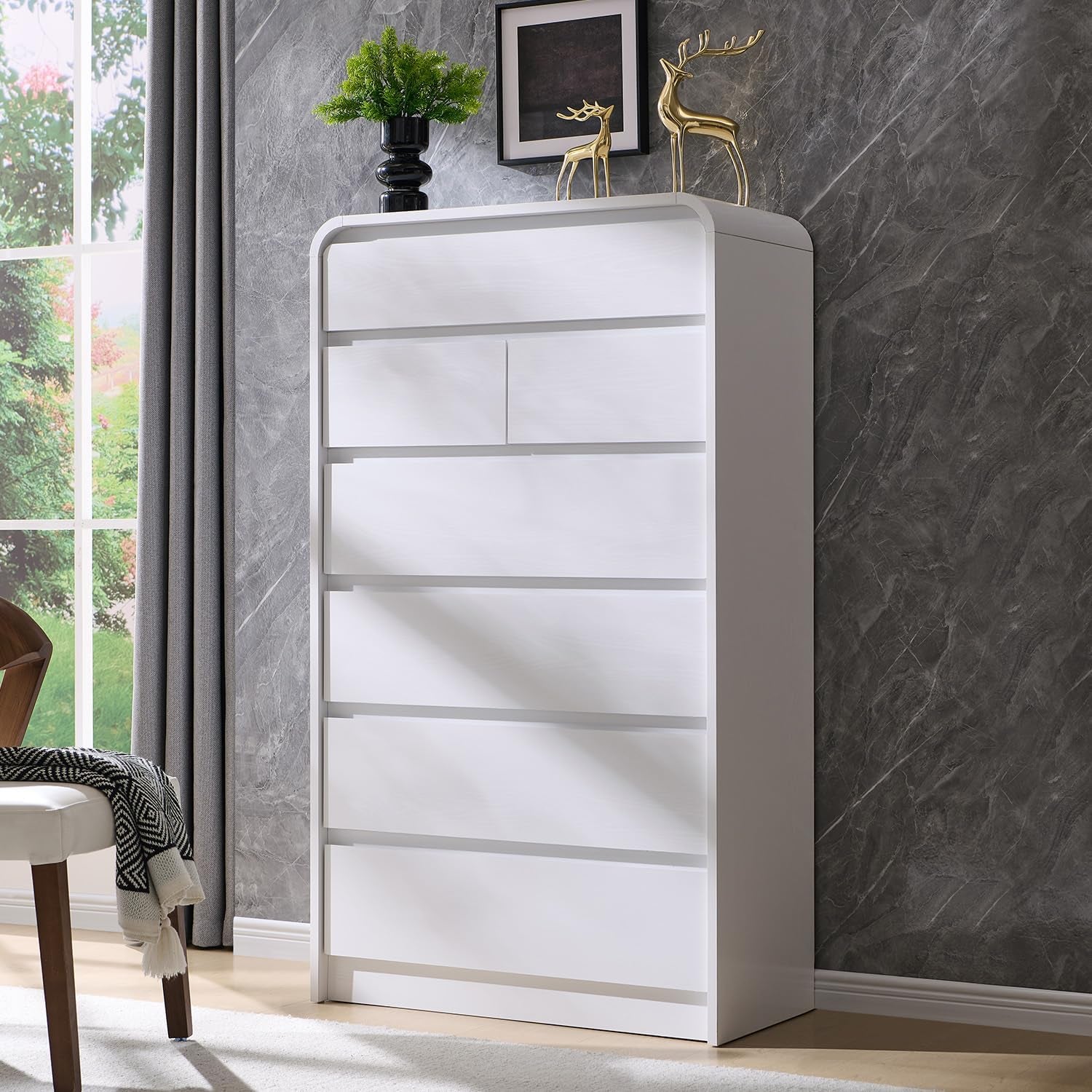 White tall dresser against a dark textured wall topped with gold deer sculptures and framed art.