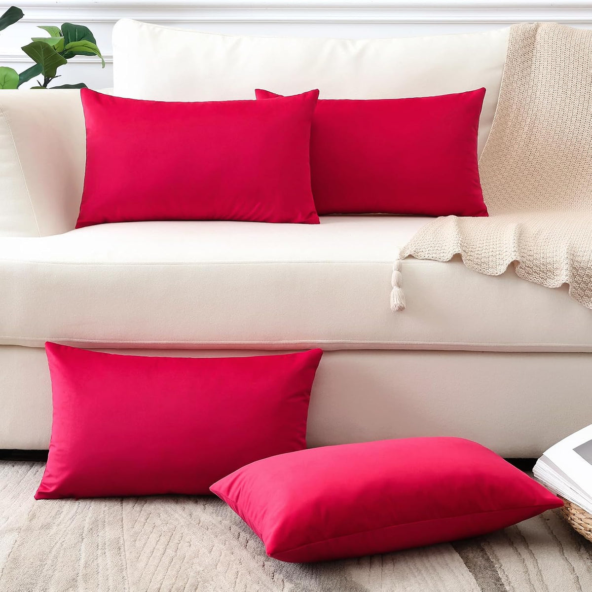 Two rectangular hot pink velvet pillows on a cream sofa with a tassel knit throw and one pillow on the floor.