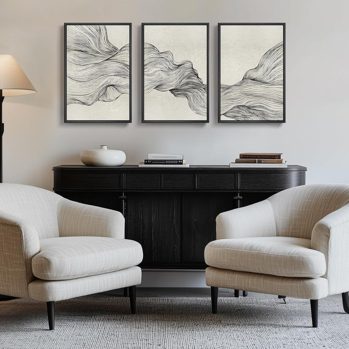 Three tall framed abstract line prints hung above a dark console between two light upholstered chairs.