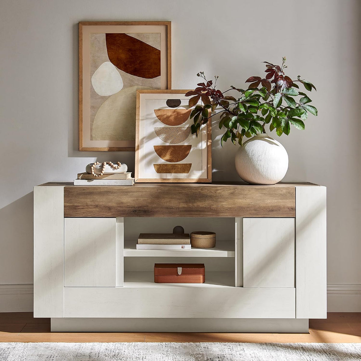 Two-tone console with white body and wood top, decorated with framed art and a round vase with greenery