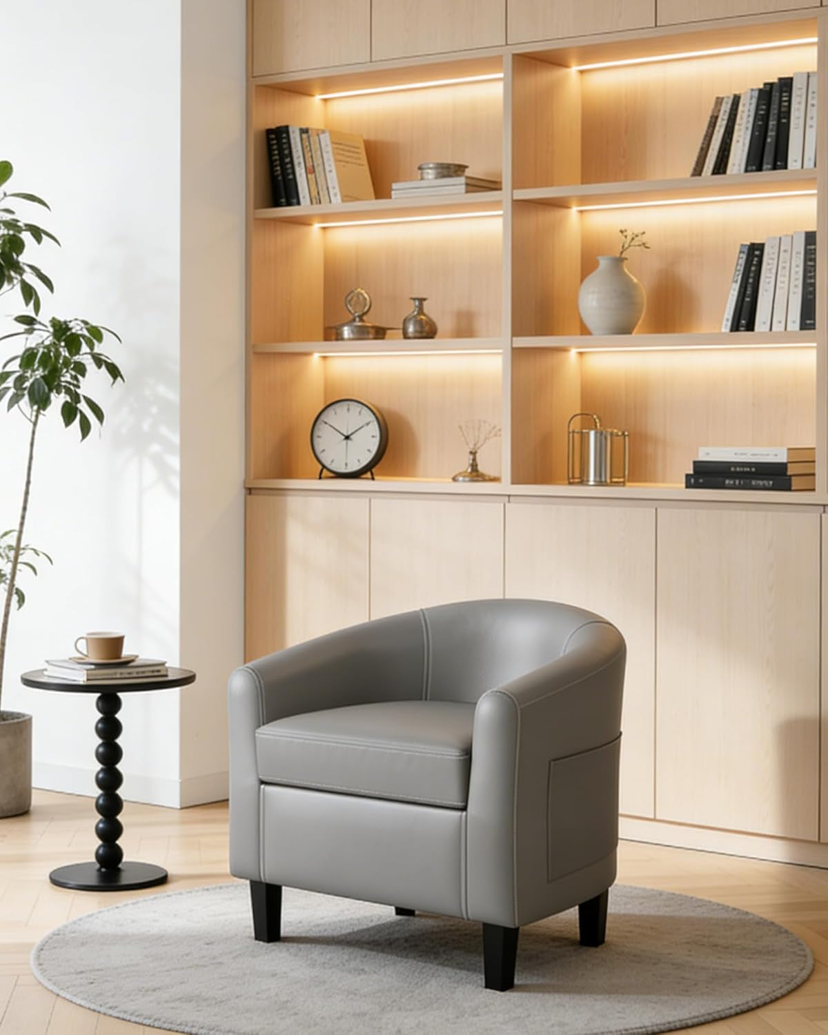 Single gray barrel armchair on a round rug placed in a bright living room with built-in wooden shelves.