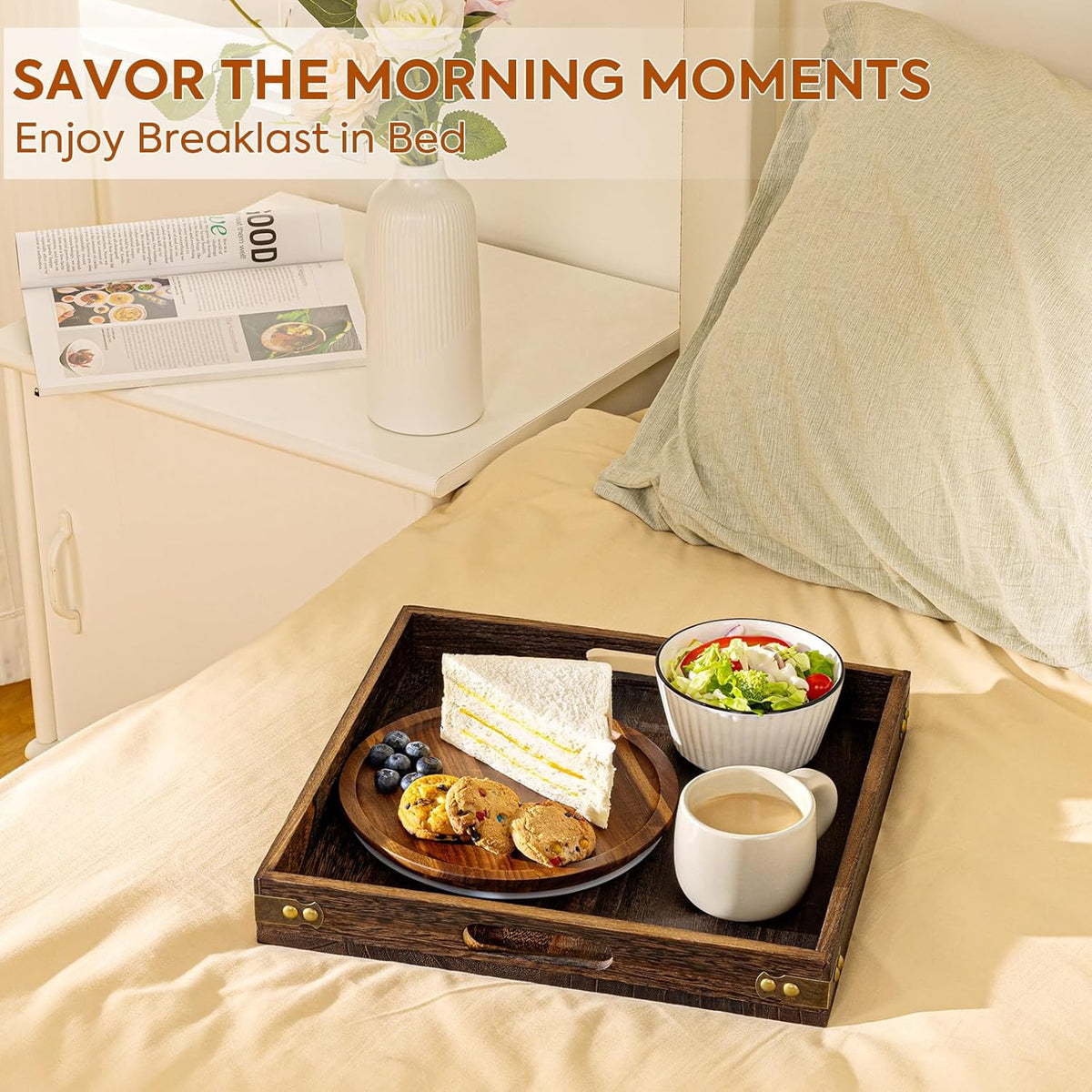Square wooden tray used on a bed beside pillows serving a sandwich, salad bowl and mug for breakfast in bed