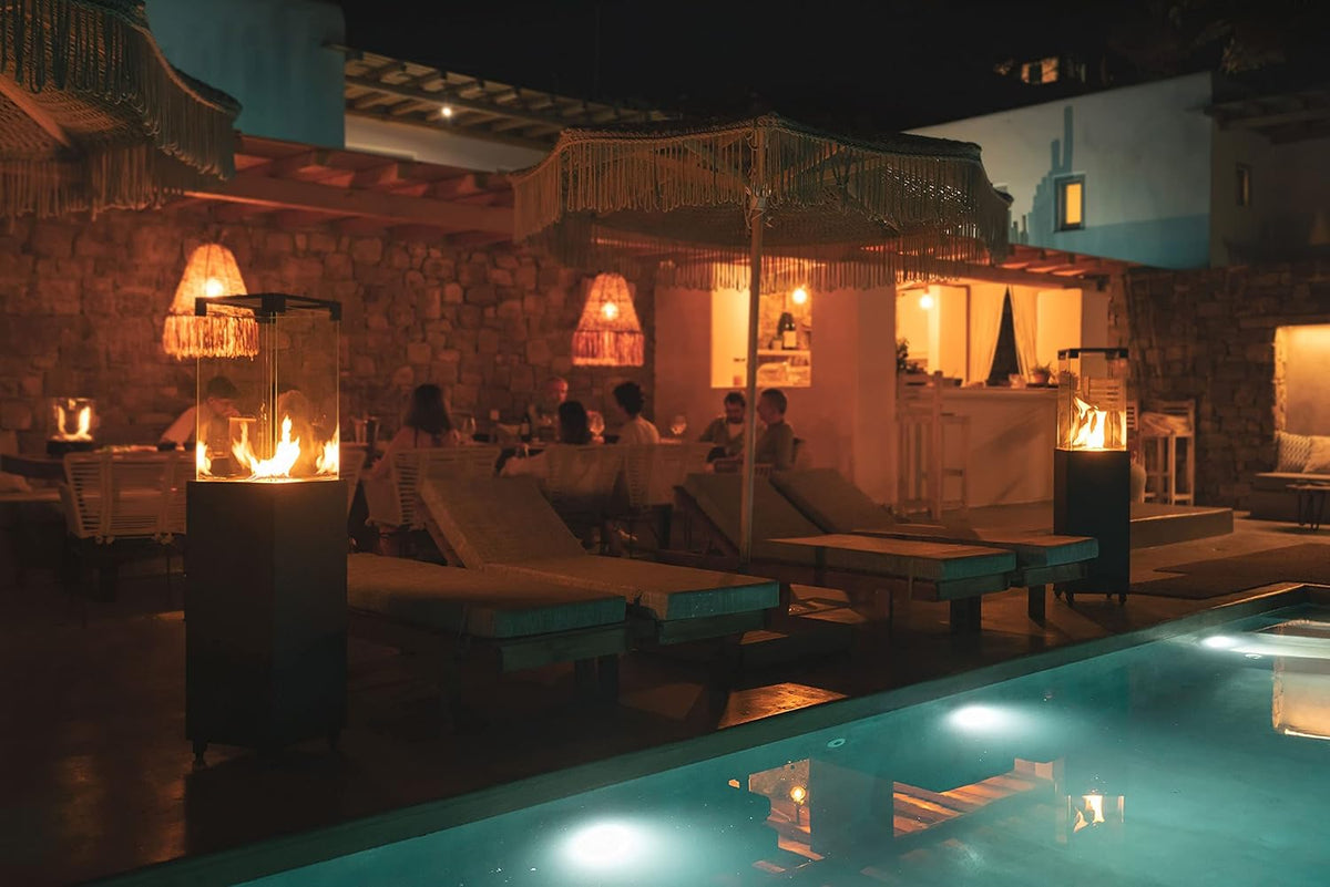 Two glass-topped patio heaters glowing beside poolside lounge chairs at night.