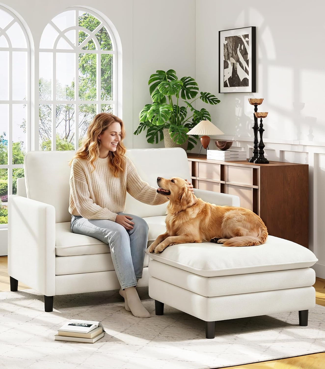 Off-white loveseat paired with an ottoman; woman pets a golden retriever on the ottoman