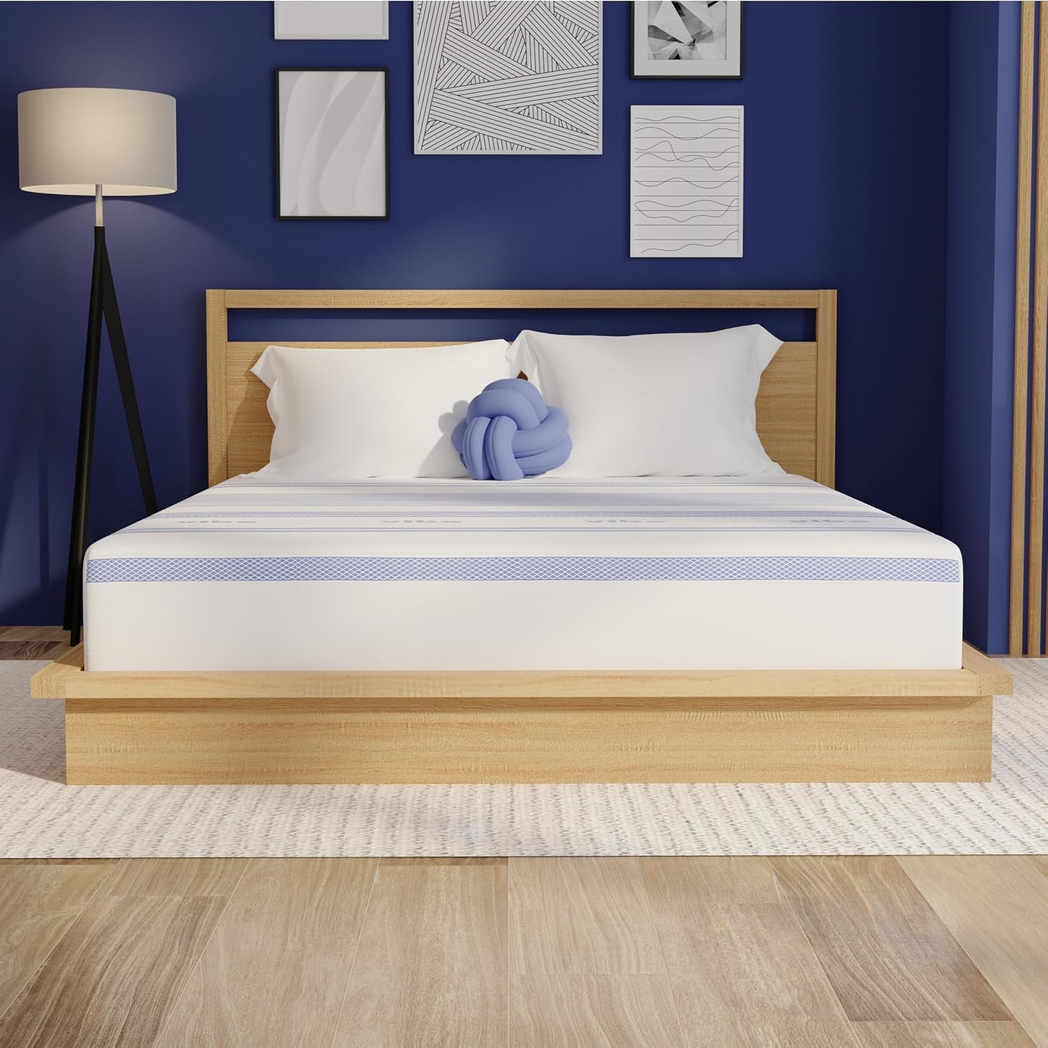 Front view of a queen mattress on a light wood platform bed against a blue wall with framed art and a floor lamp.