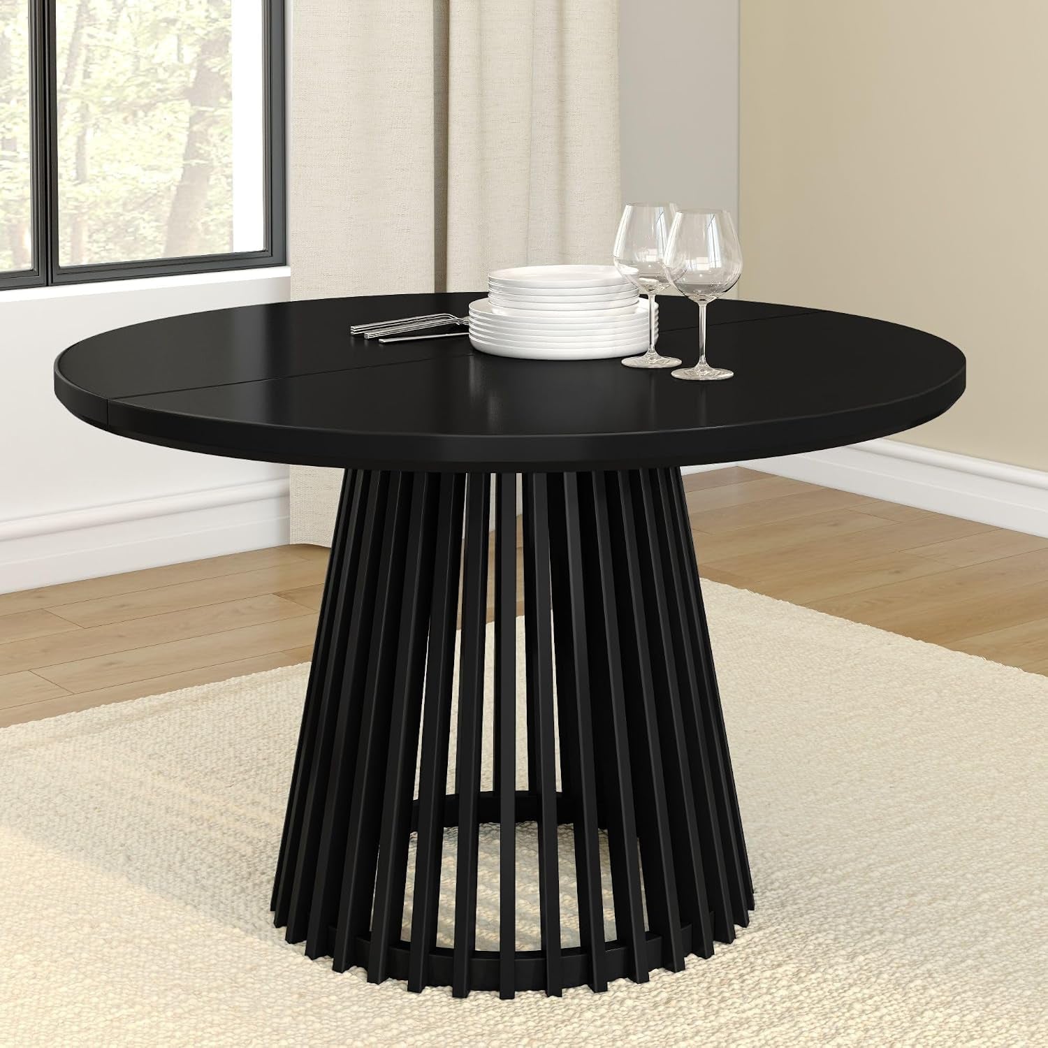 Round dining table with slatted pedestal base in black, set with stacked plates and two wine glasses