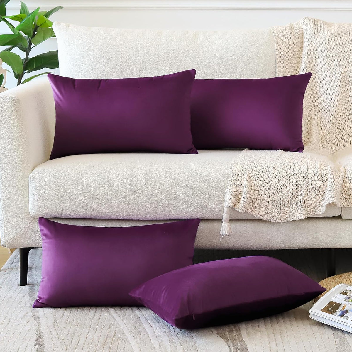 Two rectangular plum pillow covers on the sofa and two square plum covers on the floor beside a knit throw.