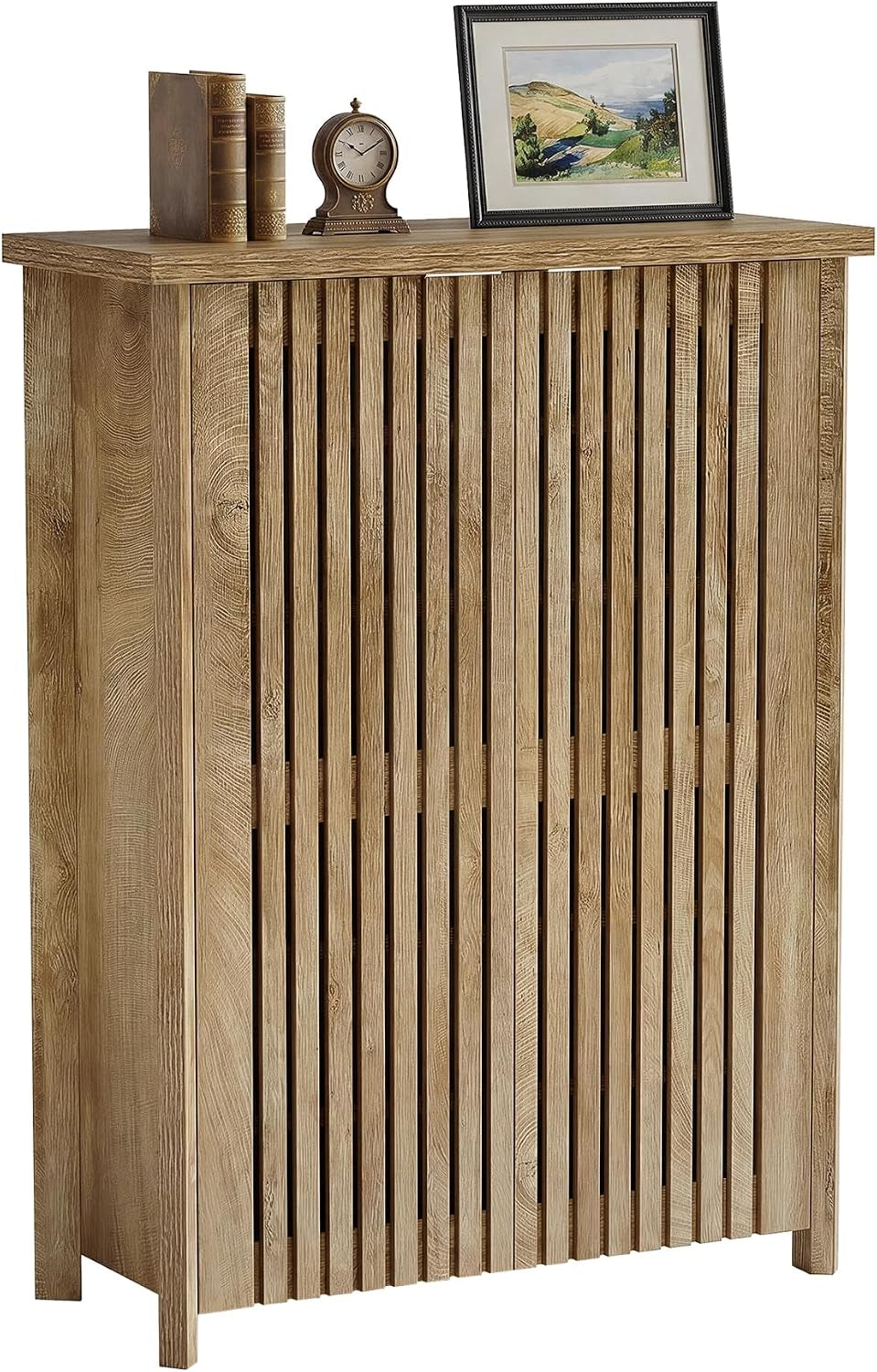 Front view of a tall wooden 6-tier shoe cabinet with vertical slatted louvered doors and books, clock, framed art on top.