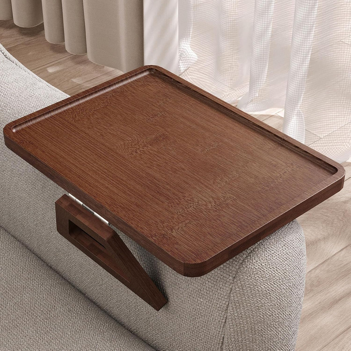 Angled close view of a dark brown wood arm tray clipped to a light-gray textured sofa, showing the clamp.