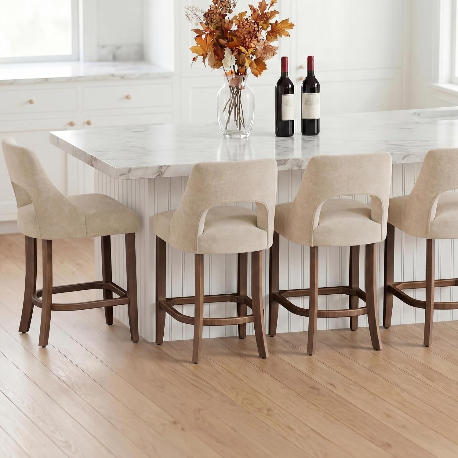 Four beige counter stools lined along an island showing matching backs and wooden footrests.