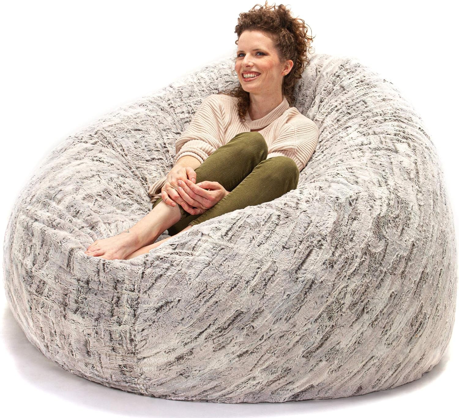 Woman curled up and smiling on a plush light gray faux-fur round bean bag against white studio background