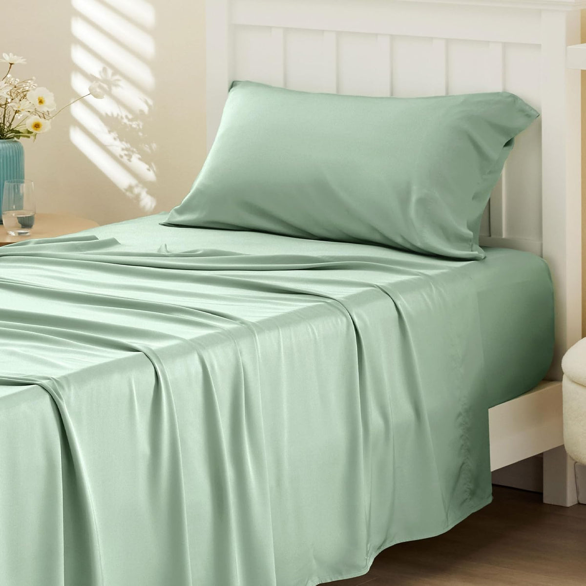 Bed with pale green silky sheets draped over mattress and a matching pillow at the headboard.