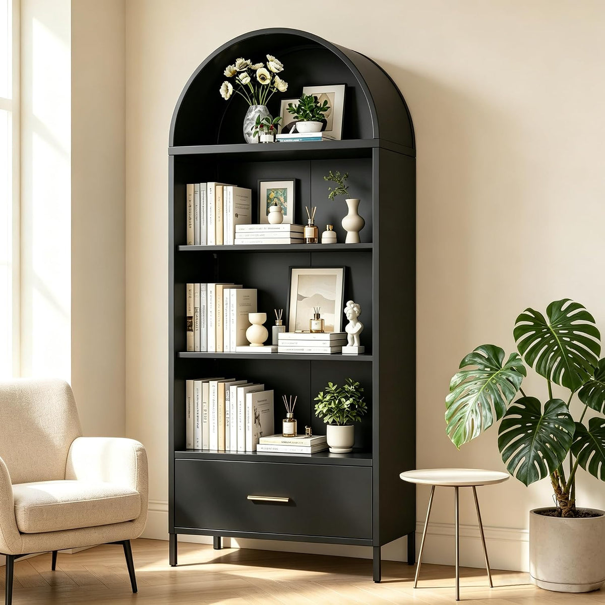 Close view of a black arched bookshelf styled with books, vases and a potted plant beside a small round table