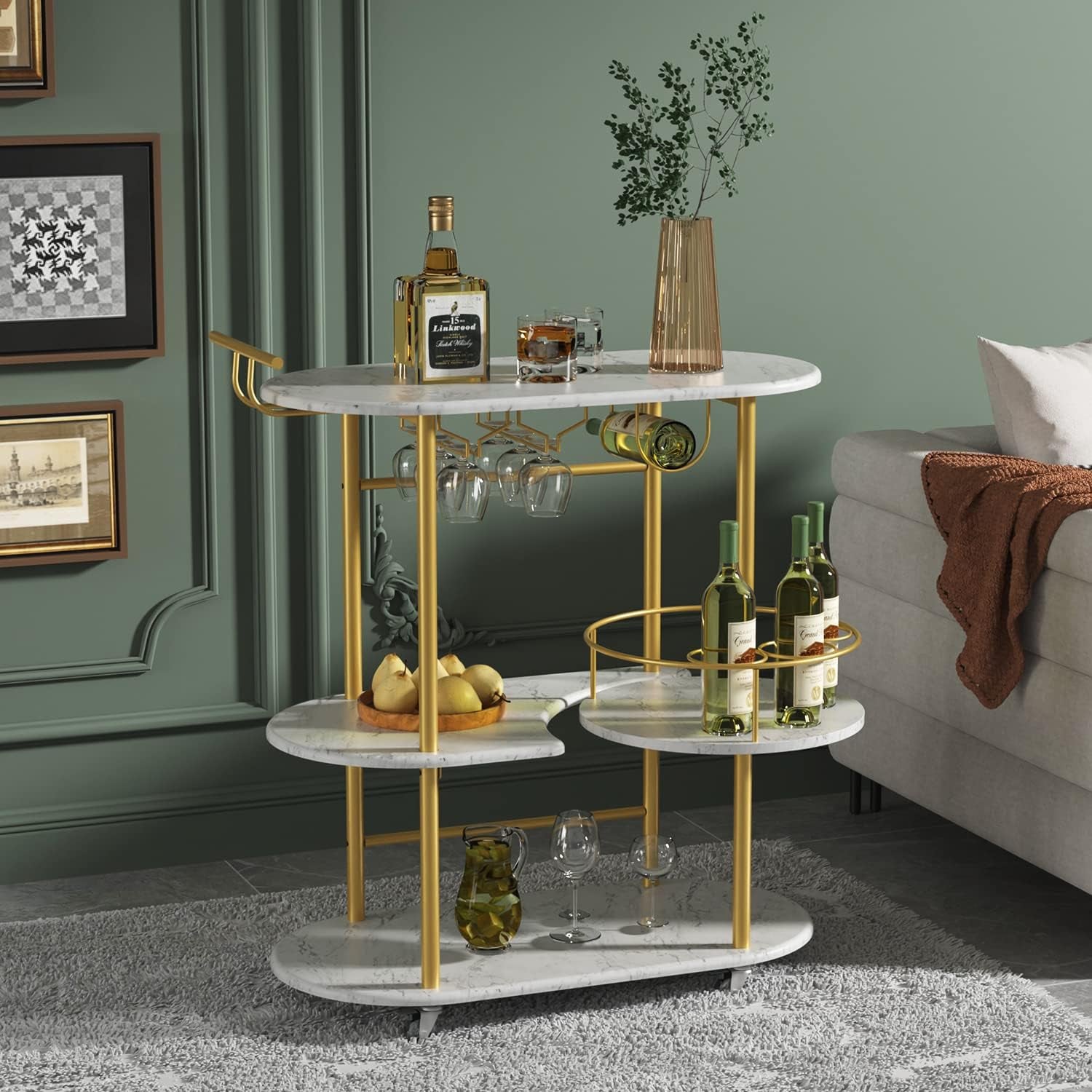 Bar cart beside a sofa in a green living room holding wine bottles, glassware and a tall vase.