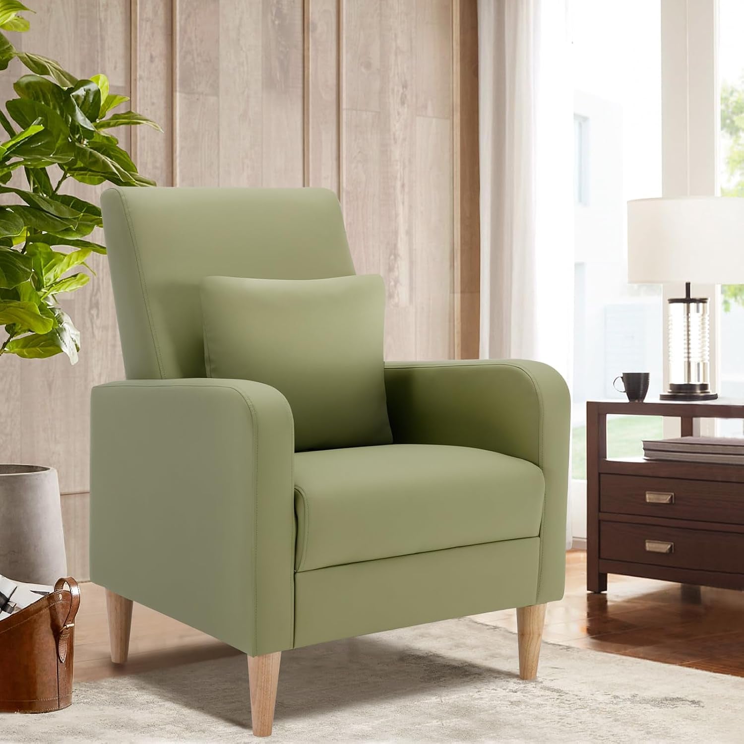 Light green high-back upholstered armchair with matching removable pillow and light wood legs beside a lamp and plant.