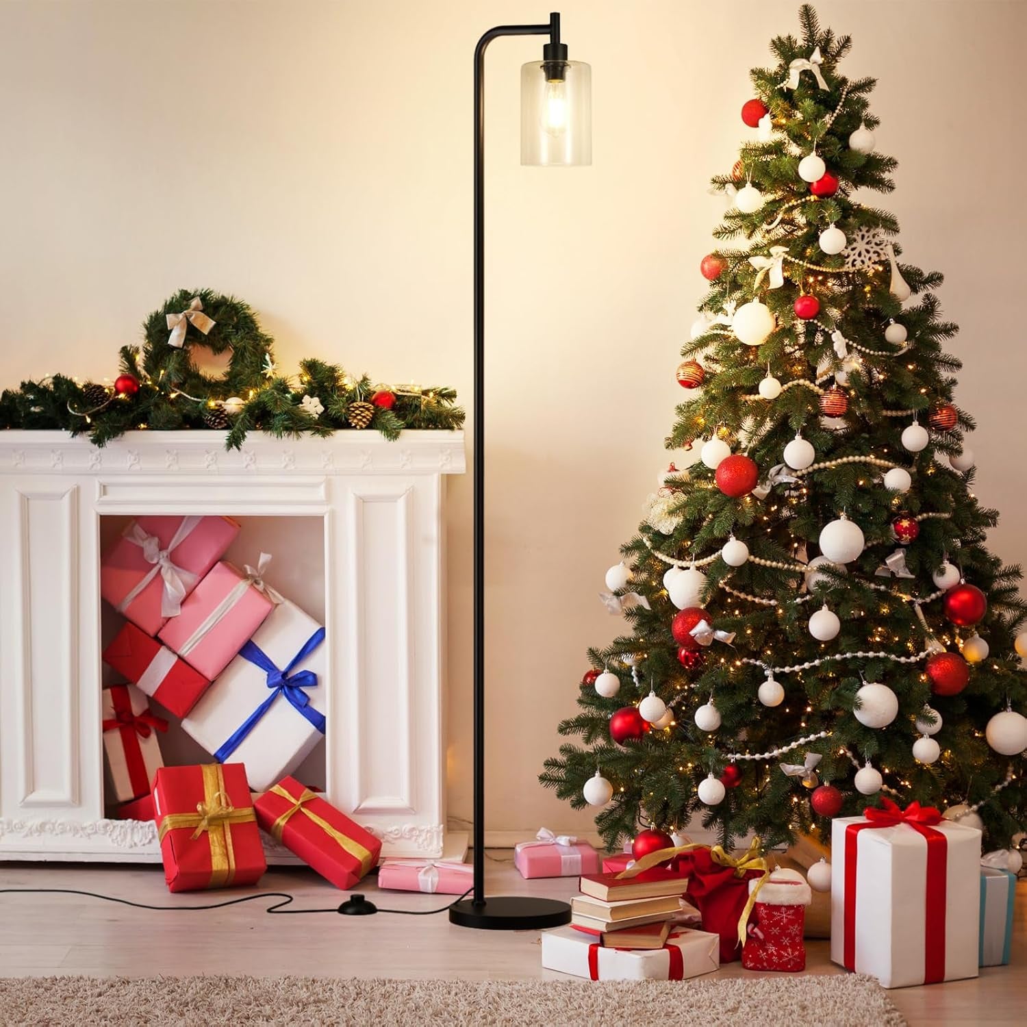 Black floor lamp with clear glass shade standing between a white mantel and a decorated Christmas tree with wrapped gifts.