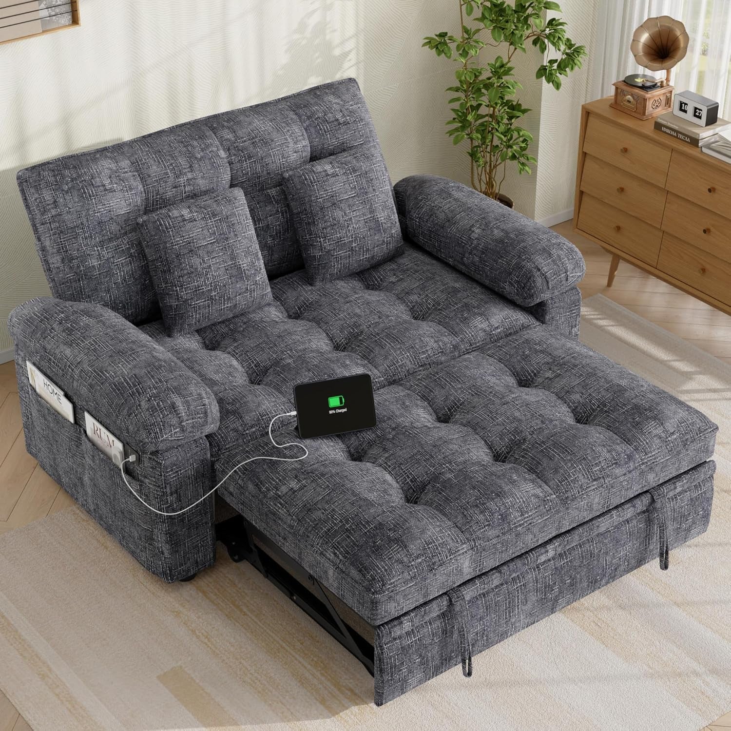 Dark gray tufted loveseat sleeper opened into a bed in a living room scene with a phone charging from the side pocket.