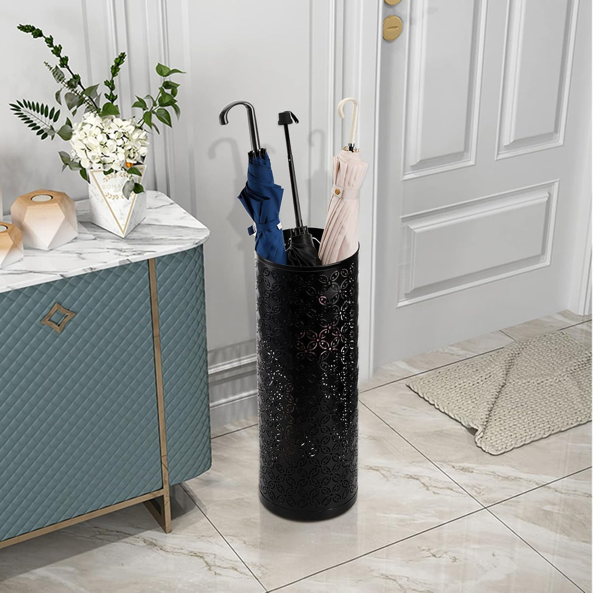 Close view of the black perforated umbrella stand by a door, holding three folded umbrellas.
