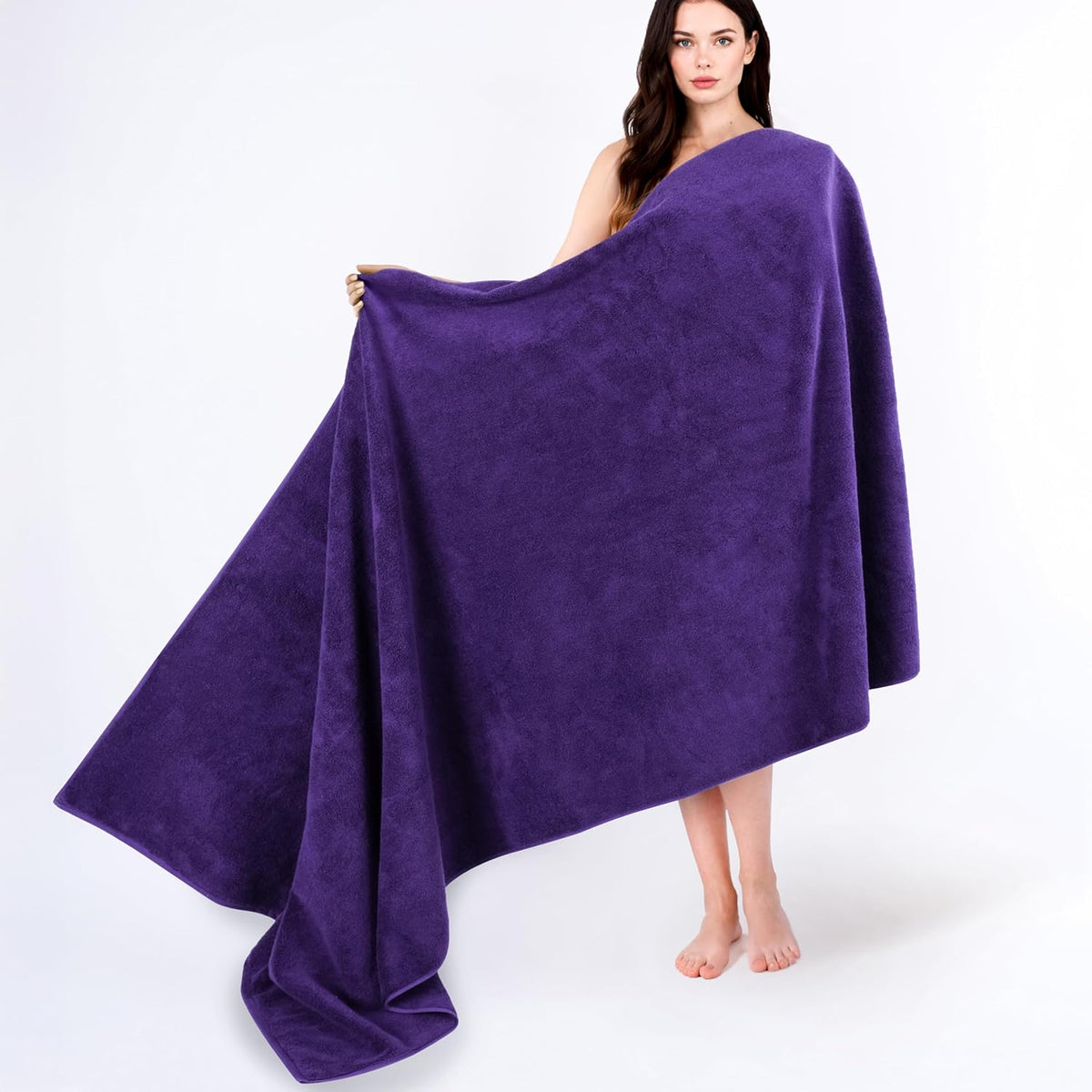 Woman standing barefoot holding and spreading a large deep purple towel across her body