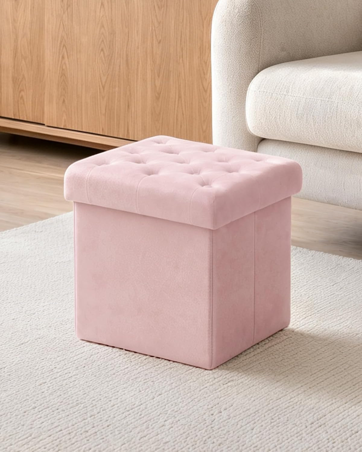 Pink velvet tufted ottoman on a rug beside a cream armchair and wood cabinet